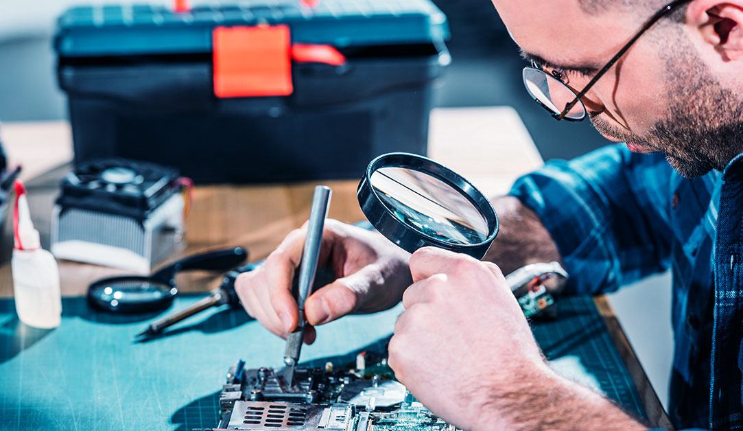 hardware-engineer-looking-at-circuit-board-through-magnifying-glass Hardware Engineer Looking at Circuit Board Through Magnifying Glass